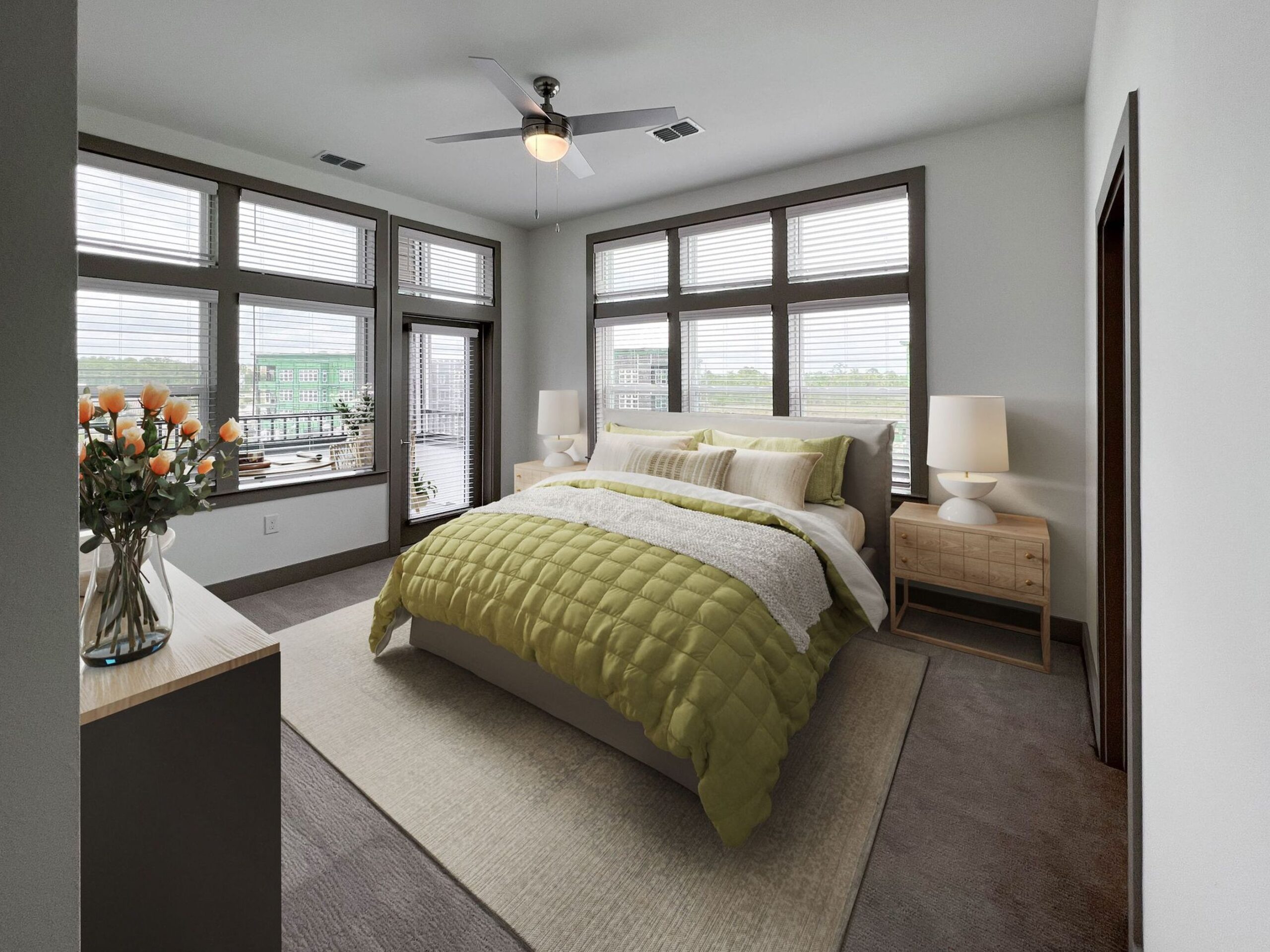 Furnished bedroom with carpet, king sized bed, large windows, and a door leading to a covered balcony at The Lucent at Sunrise.